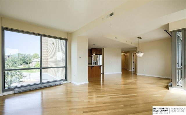 unfurnished living room with baseboard heating, lofted ceiling, and light wood-type flooring