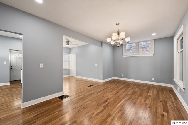 empty room with hardwood / wood-style flooring and ceiling fan with notable chandelier