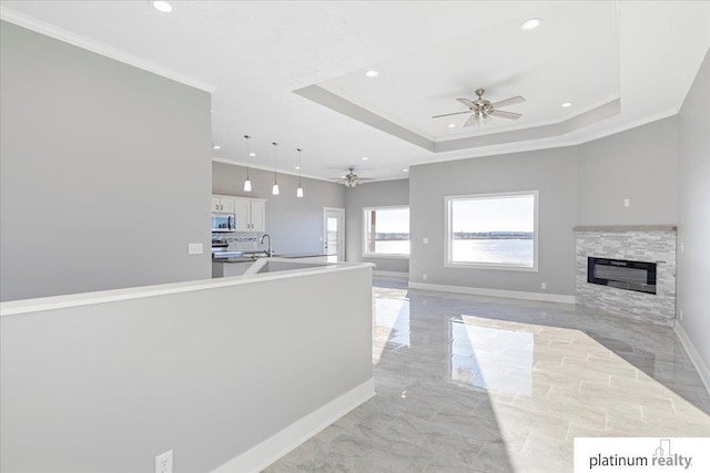 interior space with ceiling fan, a stone fireplace, crown molding, and a tray ceiling