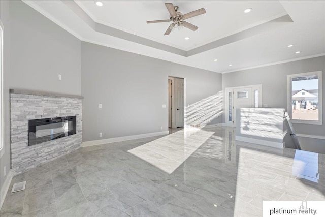 living room with ceiling fan, a stone fireplace, a raised ceiling, and ornamental molding