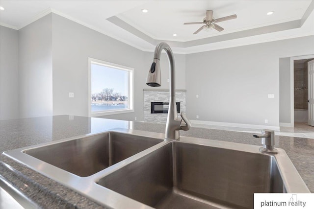 interior details featuring ornamental molding, a raised ceiling, ceiling fan, sink, and a fireplace