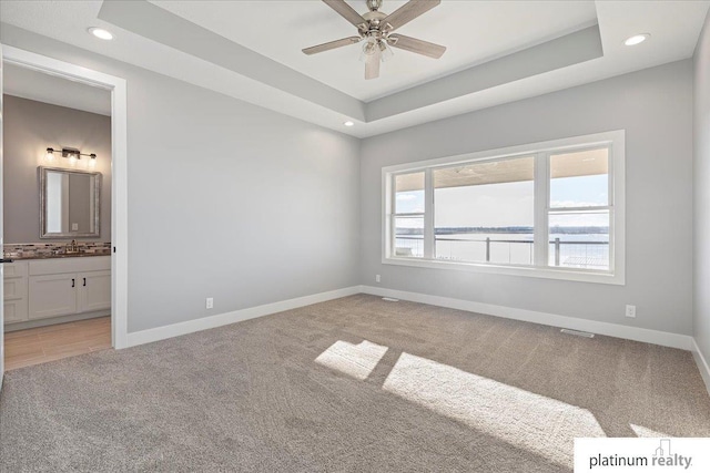 spare room featuring a raised ceiling, a water view, sink, ceiling fan, and light colored carpet