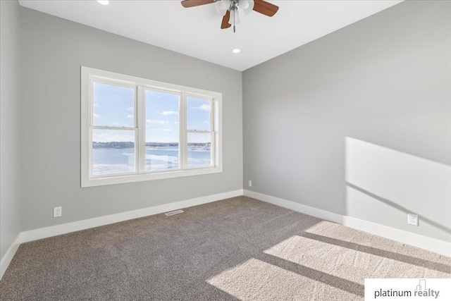 unfurnished room with carpet, ceiling fan, and a water view