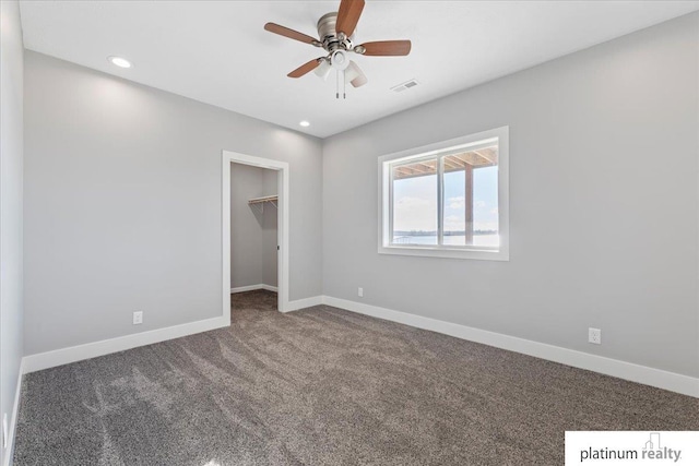 unfurnished bedroom with dark colored carpet, a closet, a spacious closet, and ceiling fan