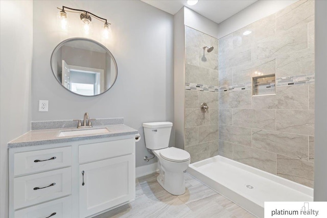 bathroom with tiled shower, vanity, and toilet