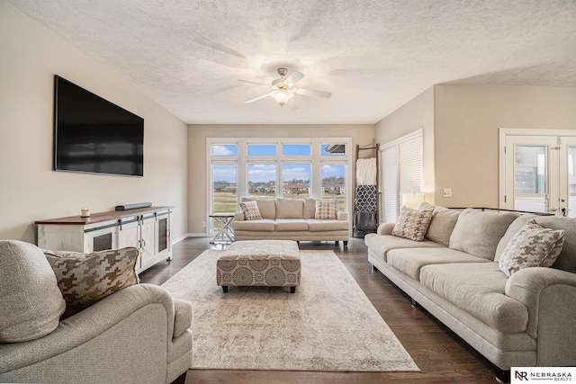 living room featuring ceiling fan, dark wood-type flooring, and a textured ceiling