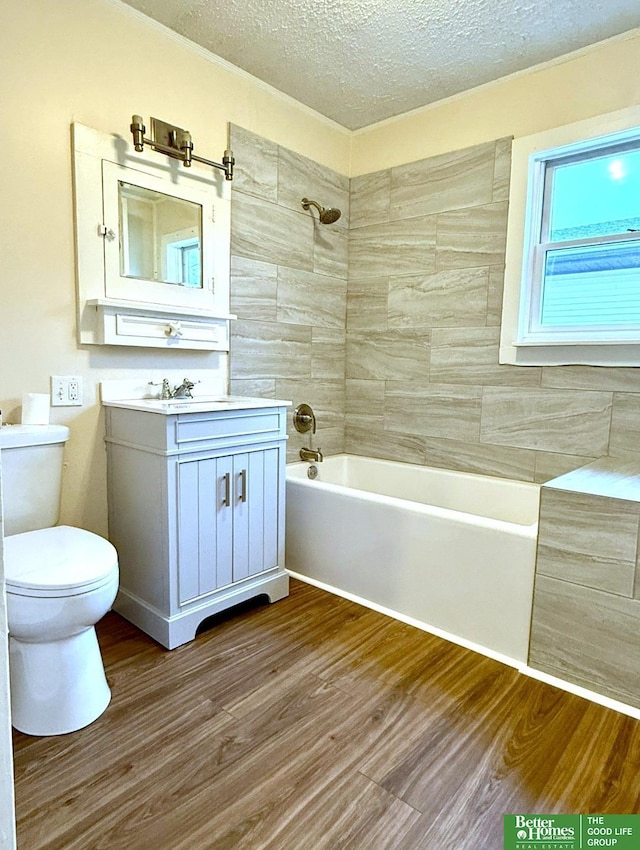 full bathroom with hardwood / wood-style floors, vanity, tiled shower / bath, toilet, and a textured ceiling