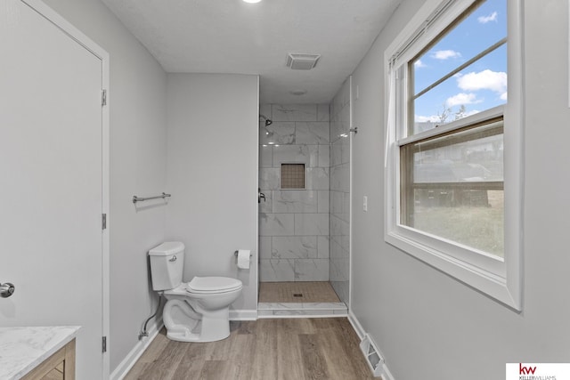 bathroom with toilet, wood-type flooring, tiled shower, and a wealth of natural light