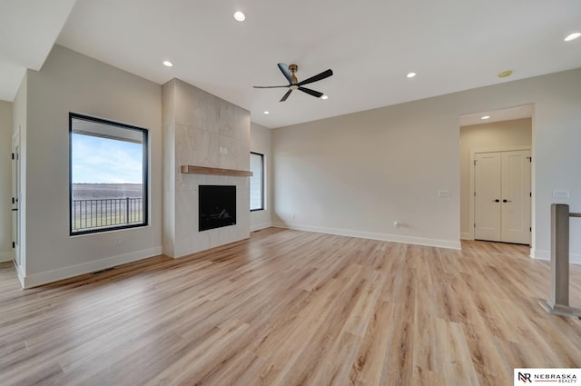 unfurnished living room featuring a tile fireplace, a wealth of natural light, ceiling fan, and light wood-type flooring