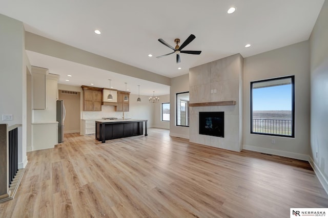 unfurnished living room with a fireplace, ceiling fan with notable chandelier, and light hardwood / wood-style flooring