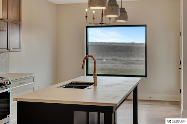 kitchen with tasteful backsplash, white cabinetry, hanging light fixtures, and an island with sink