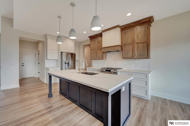 kitchen featuring white cabinets, sink, an island with sink, appliances with stainless steel finishes, and decorative light fixtures