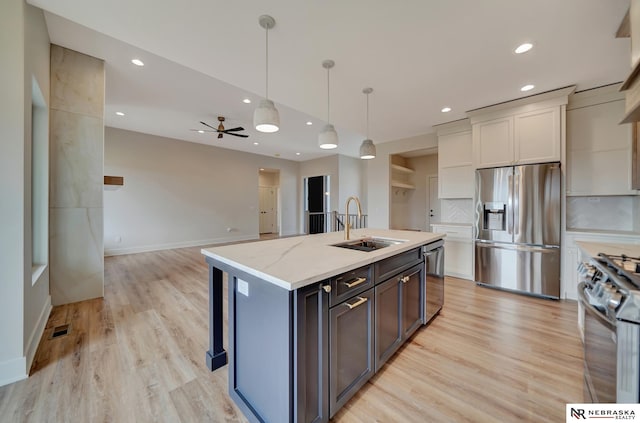 kitchen featuring a center island with sink, sink, hanging light fixtures, light stone countertops, and stainless steel appliances