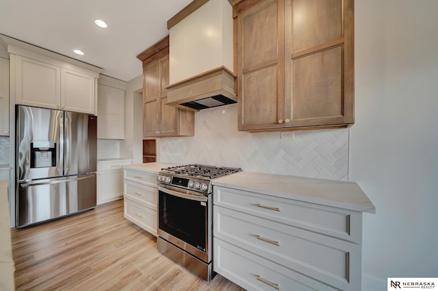 kitchen with premium range hood, white cabinets, appliances with stainless steel finishes, tasteful backsplash, and light hardwood / wood-style floors