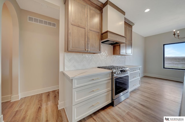 kitchen with tasteful backsplash, light stone counters, stainless steel gas range oven, custom range hood, and light hardwood / wood-style flooring