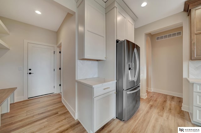 kitchen with white cabinets, stainless steel fridge, backsplash, and light hardwood / wood-style flooring