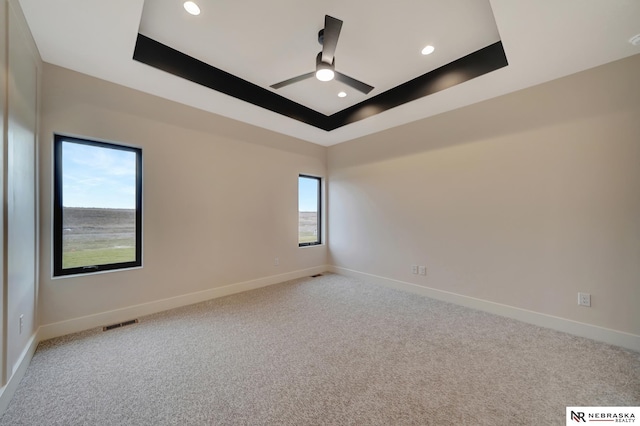 empty room featuring ceiling fan, a raised ceiling, and light colored carpet