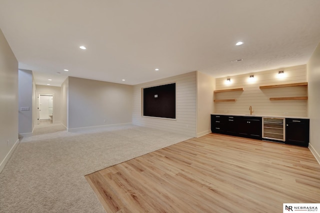 unfurnished living room with light carpet, wooden walls, beverage cooler, and wet bar