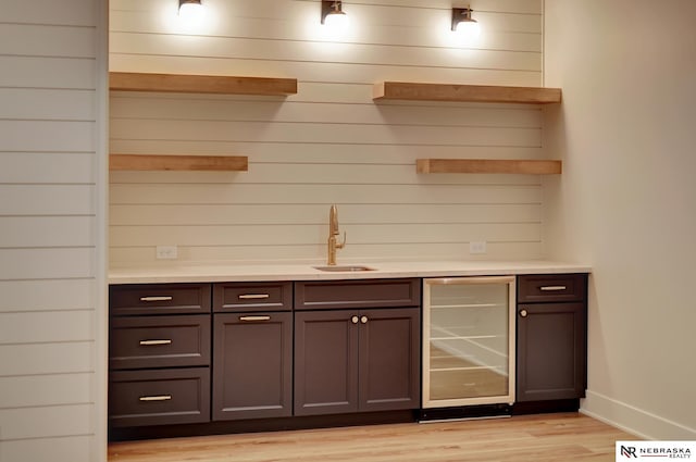 bar featuring dark brown cabinets, light wood-type flooring, wine cooler, and sink