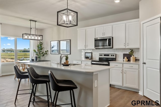 kitchen with stainless steel appliances, white cabinetry, hanging light fixtures, and an island with sink