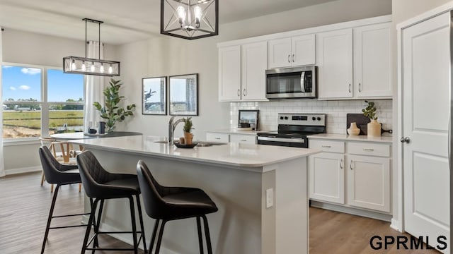 kitchen featuring decorative light fixtures, white cabinetry, stainless steel appliances, and a kitchen island with sink