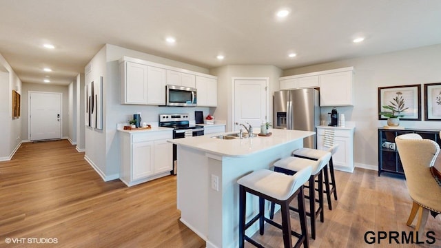 kitchen with white cabinetry, sink, stainless steel appliances, a kitchen breakfast bar, and a center island with sink