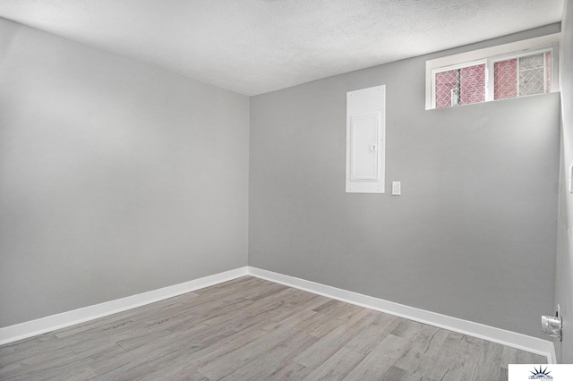 unfurnished room featuring a textured ceiling, electric panel, and light hardwood / wood-style floors