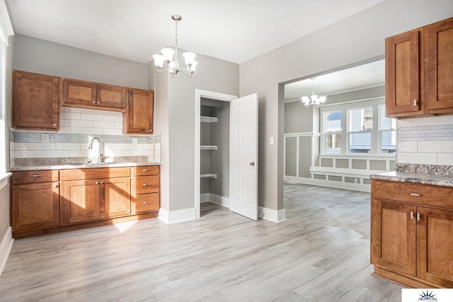 kitchen with tasteful backsplash, sink, pendant lighting, a chandelier, and light hardwood / wood-style floors