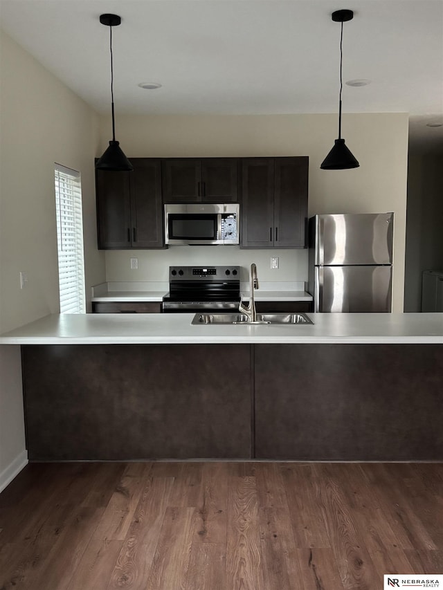 kitchen featuring radiator heating unit, sink, hanging light fixtures, appliances with stainless steel finishes, and hardwood / wood-style flooring