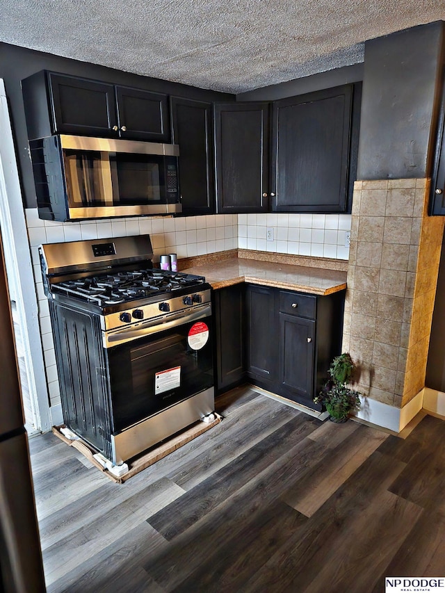 kitchen with a textured ceiling, tasteful backsplash, stainless steel appliances, and dark wood-type flooring