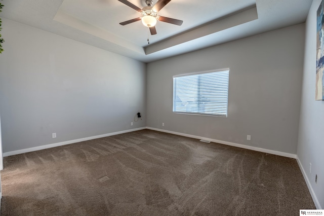 unfurnished room with a raised ceiling, dark colored carpet, and ceiling fan