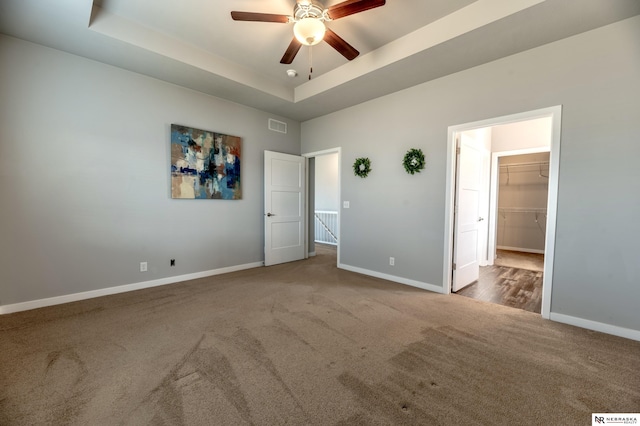 unfurnished bedroom with ceiling fan, a closet, carpet floors, a walk in closet, and a tray ceiling