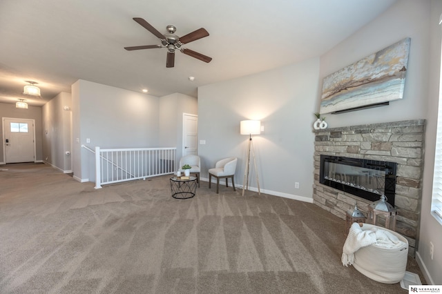 sitting room with a stone fireplace, ceiling fan, and carpet