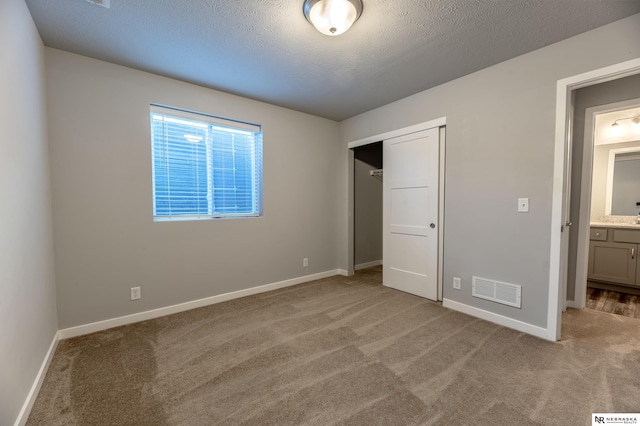 unfurnished bedroom featuring a closet, ensuite bathroom, a textured ceiling, and light colored carpet