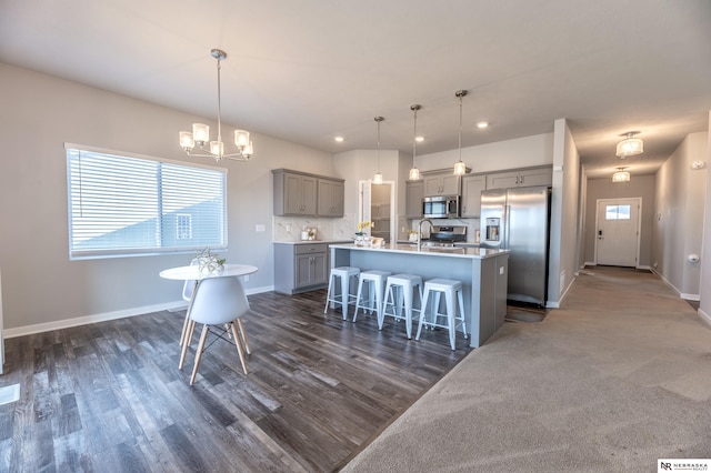 kitchen featuring stainless steel appliances, a breakfast bar area, decorative light fixtures, and an island with sink