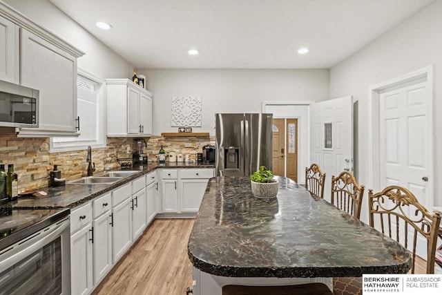 kitchen featuring appliances with stainless steel finishes, backsplash, sink, white cabinets, and a center island