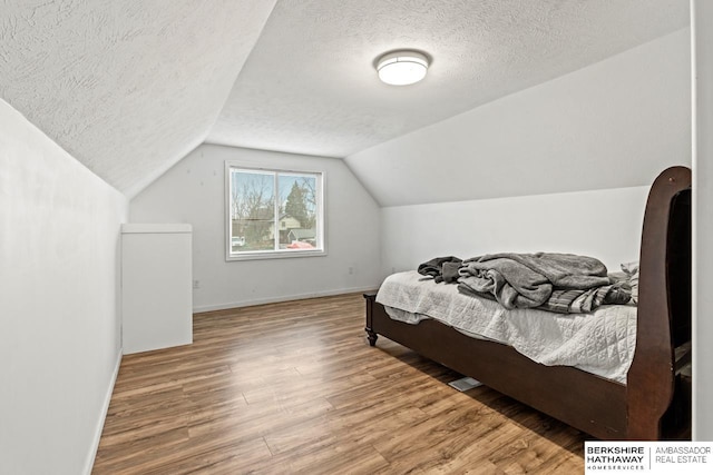 bedroom featuring a textured ceiling, hardwood / wood-style floors, and lofted ceiling