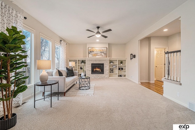 living room featuring a stone fireplace, ceiling fan, and light colored carpet