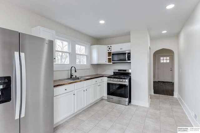 kitchen with wood counters, appliances with stainless steel finishes, sink, light tile patterned floors, and white cabinets