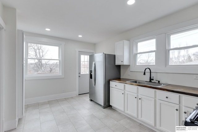 kitchen with butcher block counters, stainless steel fridge with ice dispenser, sink, and white cabinets