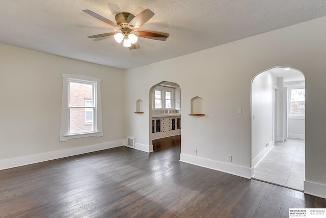 empty room with ceiling fan, dark wood-type flooring, and a textured ceiling