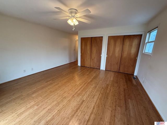 unfurnished bedroom with light hardwood / wood-style flooring, ceiling fan, and multiple closets