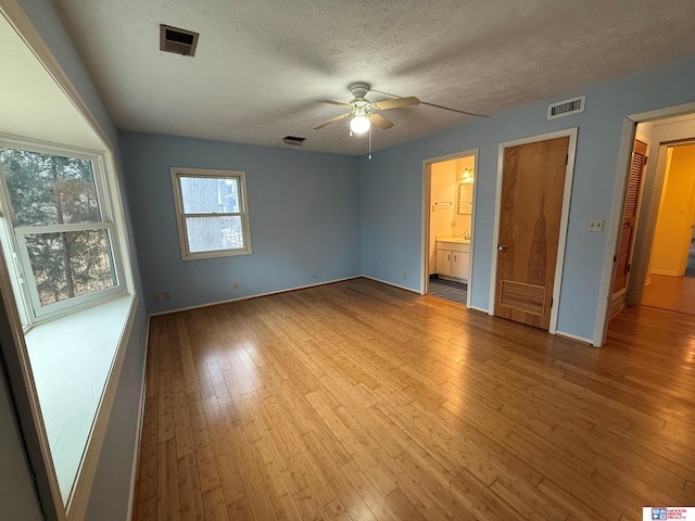 unfurnished bedroom featuring a textured ceiling, light hardwood / wood-style floors, ceiling fan, and connected bathroom