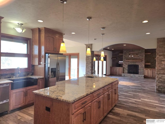 kitchen featuring sink, a fireplace, appliances with stainless steel finishes, decorative light fixtures, and a kitchen island