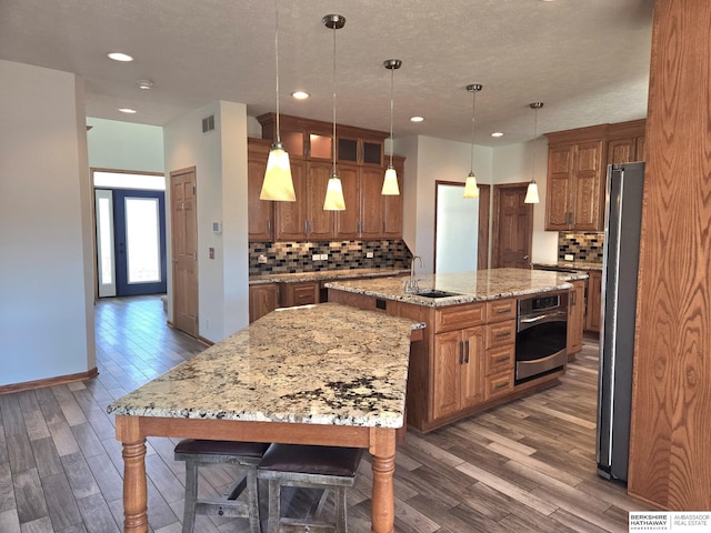 kitchen featuring light stone countertops, stainless steel appliances, tasteful backsplash, pendant lighting, and a center island with sink