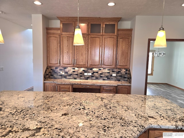 kitchen with hardwood / wood-style flooring, decorative light fixtures, light stone counters, and backsplash