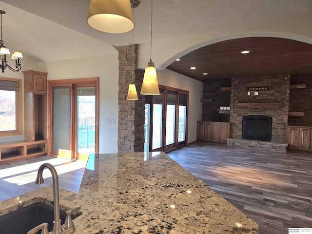 kitchen featuring dark hardwood / wood-style flooring, light stone counters, sink, a fireplace, and hanging light fixtures