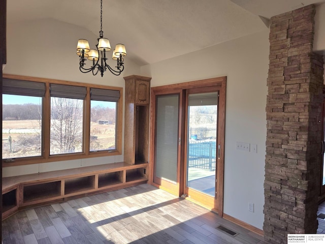 unfurnished dining area featuring decorative columns, light hardwood / wood-style floors, lofted ceiling, and a chandelier