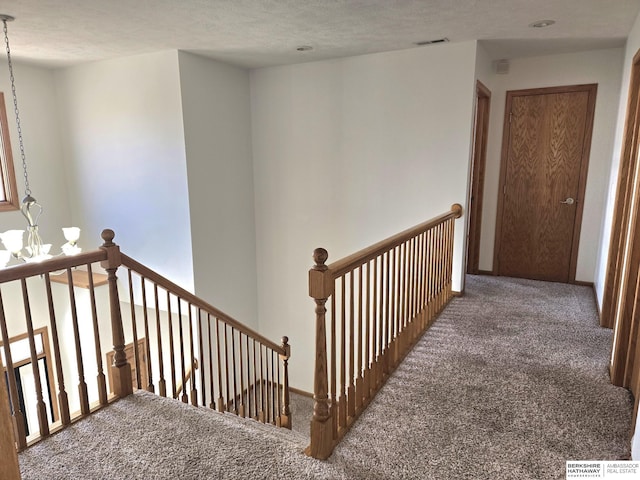 stairs with carpet, a chandelier, and a textured ceiling