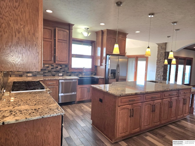 kitchen with sink, hanging light fixtures, a kitchen island, light stone counters, and stainless steel appliances